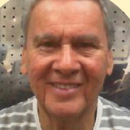 Retrato de um homem sorridente com cabelo grisalho, usando uma camiseta listrada. O fundo é desfocado.